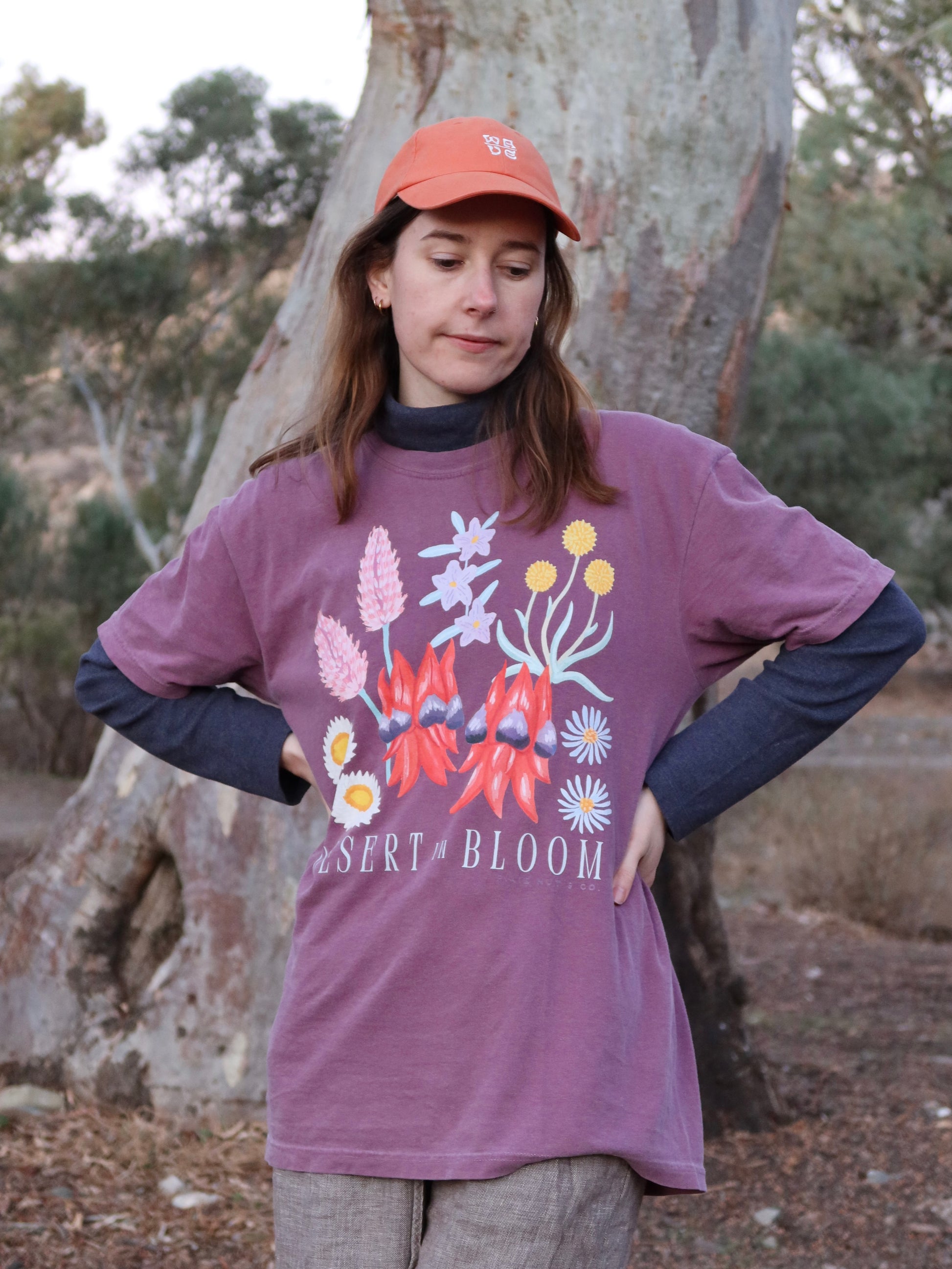 Person wearing a purple 'Desert Bloom' t-shirt outdoors near a tree